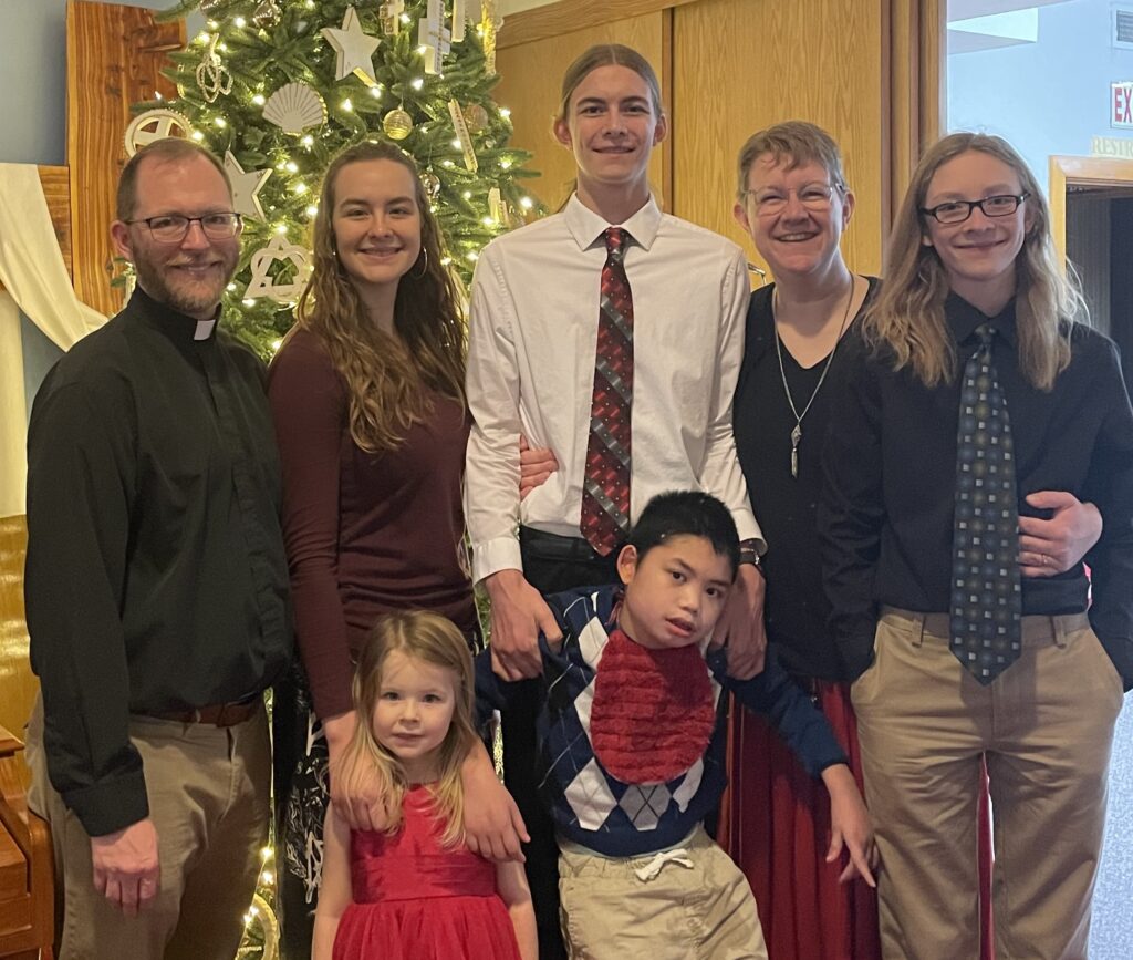 Who creates the baked goods at Loved Beyond Measure Bakery? Kristy, her husband and her five children are smiling in front of a Christmas tree. 